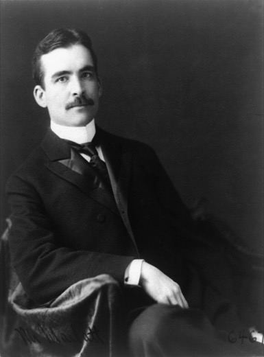 Studio portrait of a young Charles L. Marlatt with a mustache, in a dark suit and bow tie, seated