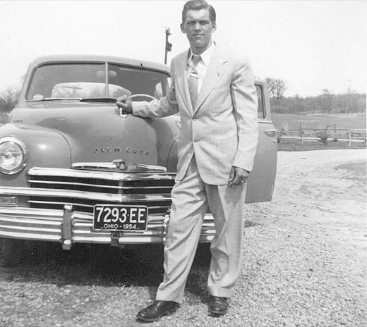 Leroy Joseph Malott in a light suit, standing beside the front of a Plymouth sedan with a 1954 Ohio license plate