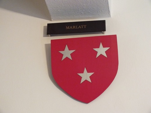 A red shield with three white stars mounted on a white wall beneath a dark nameplate reading MARLATT