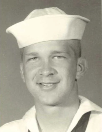 Black-and-white portrait of a smiling young sailor in a white U.S. Navy cap and dress uniform