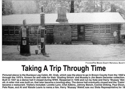Old photograph of a long log building with a stone chimney and two gasoline pumps in front, in the snow, headed Taking A Trip Through Time